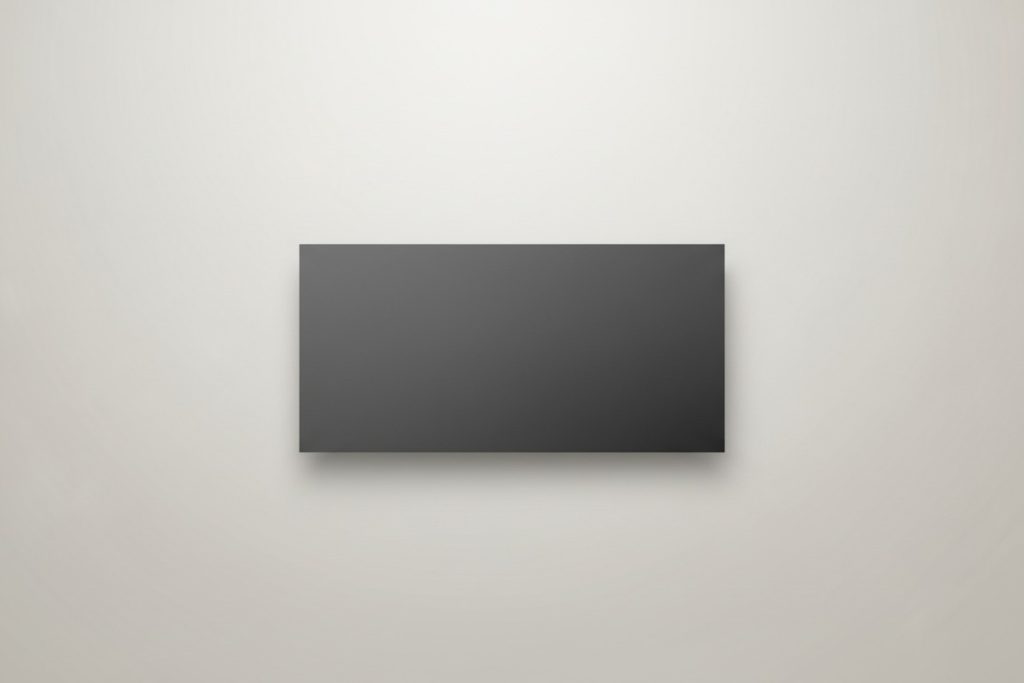 A blank, dark gray rectangular sign is mounted on a plain, light-colored wall.
